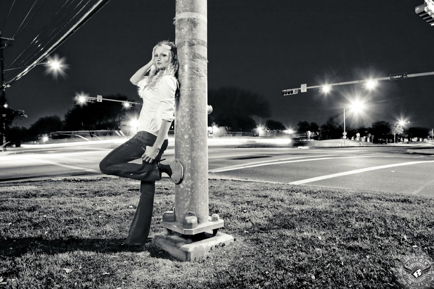 Dramatic night time senior portraits Austin of girl leaning on a traffic light pole long exposure shot.